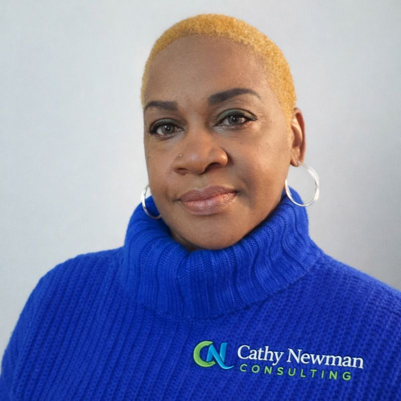 Portrait of a person with short blond hair wearing a blue turtleneck sweater featuring a logo for Cathy Newman Consulting.